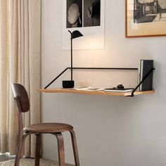 a desk with a lamp and some books on it next to a chair in front of a window