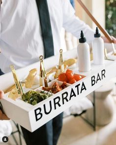 a man holding a tray with food on it that says burrata bar and condiments