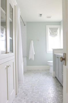 a white bathroom with hexagonal tile flooring and gray vanity cabinetry, along with an open shower door