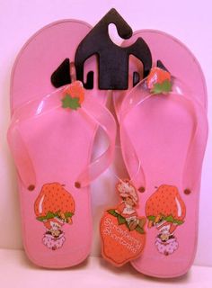 a pair of pink flip flops with strawberry shortcakes on them are hanging from a hook