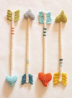 four crocheted toothbrushes are lined up on a white surface, one is shaped like a heart and the other has an arrow