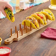 a person is holding a tortilla in front of five tacos on a wooden board