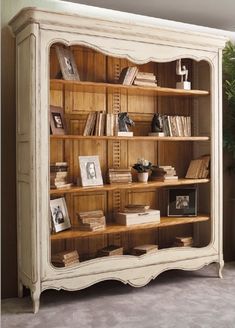 an antique bookcase with books and pictures on the shelves in front of a potted plant