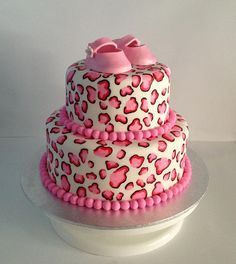 a three tiered cake decorated with pink and white leopard print icing, topped with baby booties