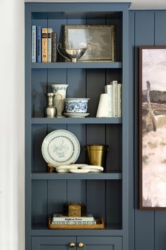 a blue bookcase filled with books next to a painting and vases on top of it