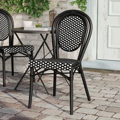 two black chairs sitting next to each other near a table and potted plant on a brick patio