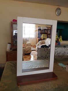 a mirror sitting on top of a table in front of a chair and bookshelf