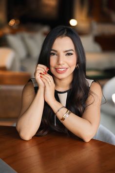 a woman sitting at a wooden table with her hands on her chin and looking into the camera