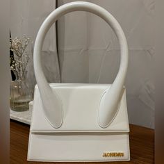 a white purse sitting on top of a wooden table next to a vase with flowers