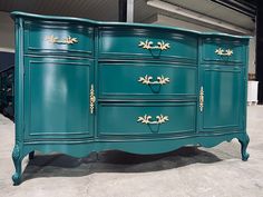 a large green dresser with gold handles and knobs on it's sides, sitting in a warehouse