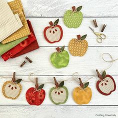 an assortment of apples hanging from clothes pins on a white wooden background with scissors and sewing needles