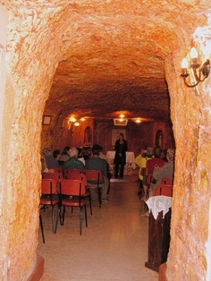 people are sitting at tables in an old cave like setting with red chairs and white tablecloths