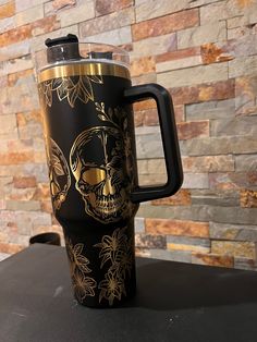 a black and gold colored coffee mug with a skull on the front is sitting on a table