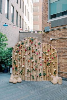 a bamboo fence with flowers on it in front of a brick wall and some plants