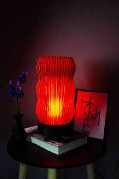 a red lamp sitting on top of a wooden table next to a book and vase