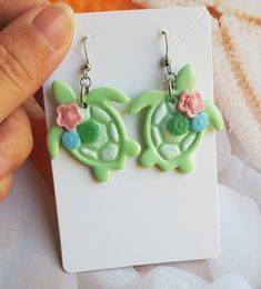 These cute Sea Turtle Earrings are handmade from polymer clay, resulting in a unique and eye-catching accessory. The earrings feature a beautifully painted shell design with delicate floral and succulent decorations in a mixture of pastel colours. Measuring approximately 3 cm in length, these earrings are the perfect size to make a statement. Despite their detailed design, they are remarkably lightweight, ensuring comfortable wear throughout the day. To add a touch of elegance and durability, ea Playful Multicolor Flower Earrings As Gift, Cute Green Hand Painted Jewelry, Hand Painted Multicolor Cute Earrings, Whimsical Resin Jewelry With Ear Wire, Green Novelty Resin Jewelry, Handmade Polymer Clay Flower Earrings For Gift, Handmade Novelty Resin Jewelry, Playful Handmade Turquoise Jewelry, Hand Painted Green Earrings In Polymer Clay