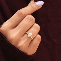 a woman's hand wearing a gold ring with a pear shaped diamond on it