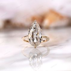 an engagement ring with a pear shaped diamond in the center on a white marble surface