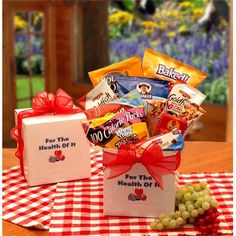 a gift box filled with candy sits on a checkered tablecloth next to grapes