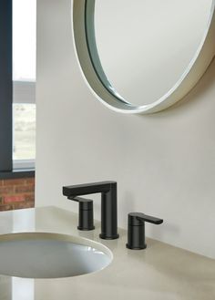 a bathroom sink with two faucets and a round mirror