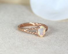 a gold ring with an opal stone in the center on a white surface next to a flower