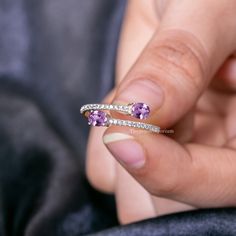 a woman's hand holding an open ring with purple stones and diamonds on it