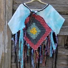 a crocheted top with fringes hanging on a wooden wall next to a piece of wood