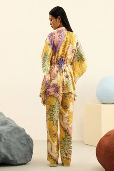 Firefly mulberry silk kimono top with all over floral vintage print, elasticated waist and front tasselled tie-up. Paired with printed high waisted straight fit trousers.
Components: 2
Pattern: Printed
Type Of Work: Vintage Floral Print
Neckline: Collar
Sleeve Type: Kimono Sleeves
Fabric: Mulberry Silk
Color: Yellow
Other Details: 
Embellished tassels
Asymmetric hem
Side pockets on trousers
Closure:
Top: Front drawstring tie-up and front buttons
Trousers: Half elasticated waistband
Occasion: Wor Summer Silk Daywear Sets, Silk Summer Sets For Daywear, Summer Silk Sets For Daywear, Silk Kimono With Floral Print For Loungewear, Spring Silk Set With Kimono Sleeves, Silk Set With Kimono Sleeves For Spring, Silk Summer Sets With Kimono Sleeves, Spring Vacation Silk Sets, Vacation Sets In Silk For Spring