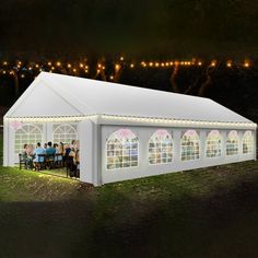 a large white tent with people standing around it at night in front of string lights