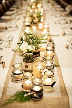 a long table is set with candles and flowers in mason jar vases on it