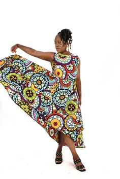 A woman posing in a bright multi-colored African print high-low maxi dress. Flowy Multicolor Floral Print Sleeveless Dress, Multicolor Printed Maxi Sleeveless Dress, Multicolor Flowy Sleeveless Dress, Bohemian Multicolor Printed Sleeveless Dress, Multicolor Bohemian Printed Sleeveless Dress, Beach Dress With Printed Asymmetrical Hem, Bohemian Sleeveless Multicolor Print Dress, Beach Dresses With Printed Asymmetrical Hem, Beach Dress With Asymmetrical Hem And Printed Design