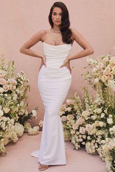 a woman standing in front of flowers wearing a white gown with straps and open back