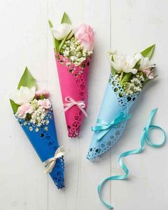 three paper cones with flowers in them on a white table next to a blue ribbon