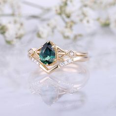 a close up of a ring with a green stone in the middle and white flowers behind it