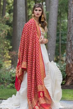 a woman in a white dress and red shawl is walking through the woods with her hands on her hips