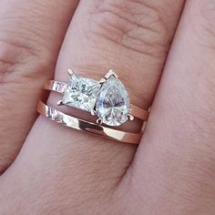 a woman's hand with two engagement rings on top of her finger and the ring has a pear shaped diamond in it