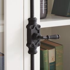 an iron door handle on the side of a white bookcase with books behind it