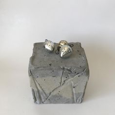 two small silver bells sitting on top of a cement block in front of a white background