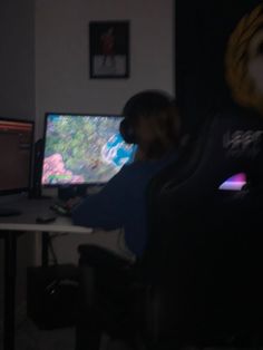 two people sitting in front of computer screens on desks, one person is playing video games