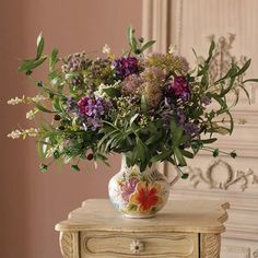 a vase filled with lots of flowers on top of a wooden table next to a dresser