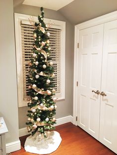 a decorated christmas tree in the corner of a room with white shutters and wooden floors