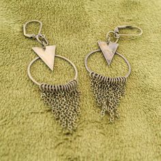 These fun geometric charm earrings come in a subtle antique brass finish. Each earring has a cascade of dainty chains hanging from a hoop in a chainmail reminiscent pattern. These bold and lively earrings are sure to make an impression. With a matching necklace available, this would make a fabulous gift set! -Geometric triangle and hoop charm -hanging chain accents -Antique brass finish -Leverback earring closure Nickel-free Bronze Dangle Hoop Earrings, Bronze Nickel-free Dangle Hoop Earrings, Minimalist Metal Dangle Chandelier Earrings, Nickel-free Geometric Brass Earrings, Brass Jewelry With Dangling Charms, Bronze Metal Dangle Chandelier Earrings, Brass Dangling Charms Drop Earrings, Bohemian Triangle Nickel-free Earrings, Geometric Nickel-free Metal Earrings