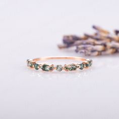 a gold ring with green stones on it and lavender flowers in the background, sitting next to each other