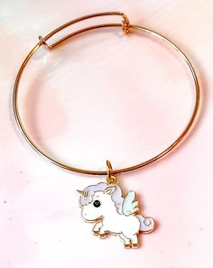 The Pastel Unicorn Gold Bangle Enamel Charm Bracelet is a whimsical and delightful piece of jewelry that adds a touch of magic to your wrist. Crafted with attention to detail, this bracelet features a slim and elegant gold bangle adorned with a enchanting pastel unicorn charm. The charm is beautifully designed with colorful enamel detailing, creating a vibrant and playful look. The bangle is adjustable to fit different wrist sizes, ensuring a comfortable and secure fit. This bracelet is perfect Unicorn Charm Bracelet, Cute Adjustable Charm Bangle Bracelet, Cute Adjustable Bangle Charm Bracelet, Adjustable Novelty Jewelry For Best Friend Gift, Cute Friendship Bangle Jewelry, White Unicorn Print Jewelry For Gifts, White Unicorn Print Jewelry For Gift, Cute Bangle Jewelry For Birthday, Cute Bangle For Birthday