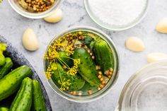 cucumbers and other vegetables are in glass bowls on a marble surface with salt and pepper