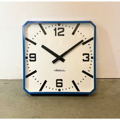 a blue and white clock sitting on top of a floor next to a wall with numbers