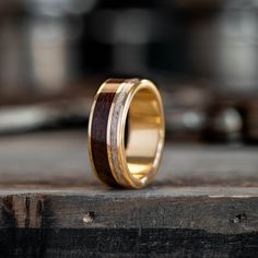 a wooden ring with gold inlays sits on top of a piece of wood