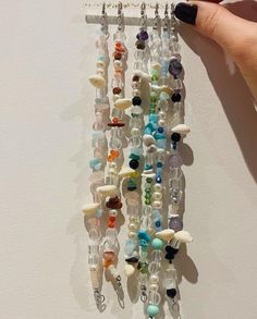 a hand holding a bunch of beads and charms on a wall hanging from it's side