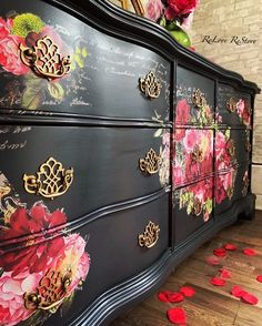 a black dresser with flowers painted on it and red petals scattered around the top drawer