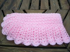 a pink crocheted blanket sitting on top of a wooden bench